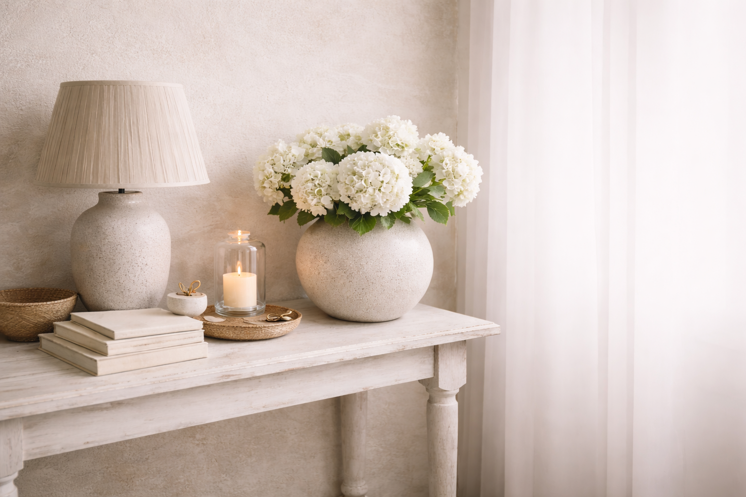 White vase with flowers on a table next to a lamp and books in a softly lit room.